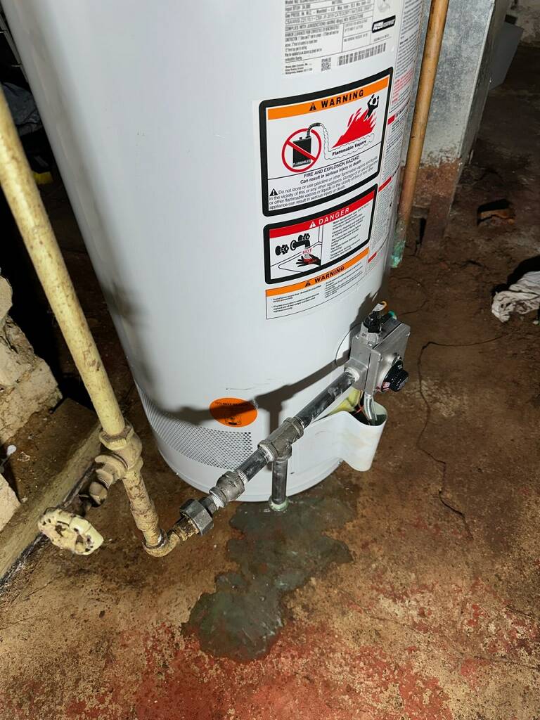 Old failing water heater with rusty pipes on stained basement floor