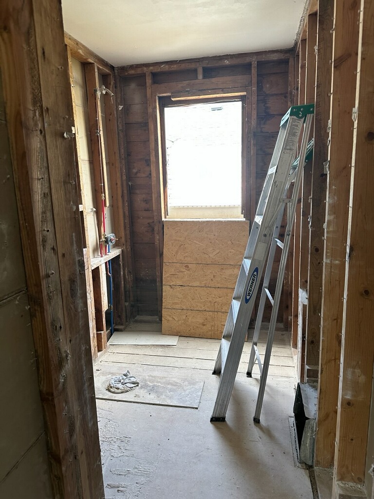 Half bath gutted to studs with exposed framing and rough plumbing
