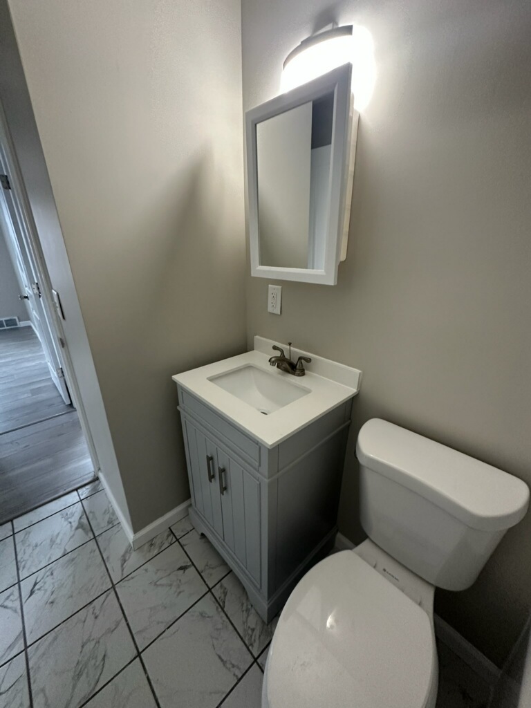 Finished half bath with new vanity, mirror, toilet, and marble-look tile floor