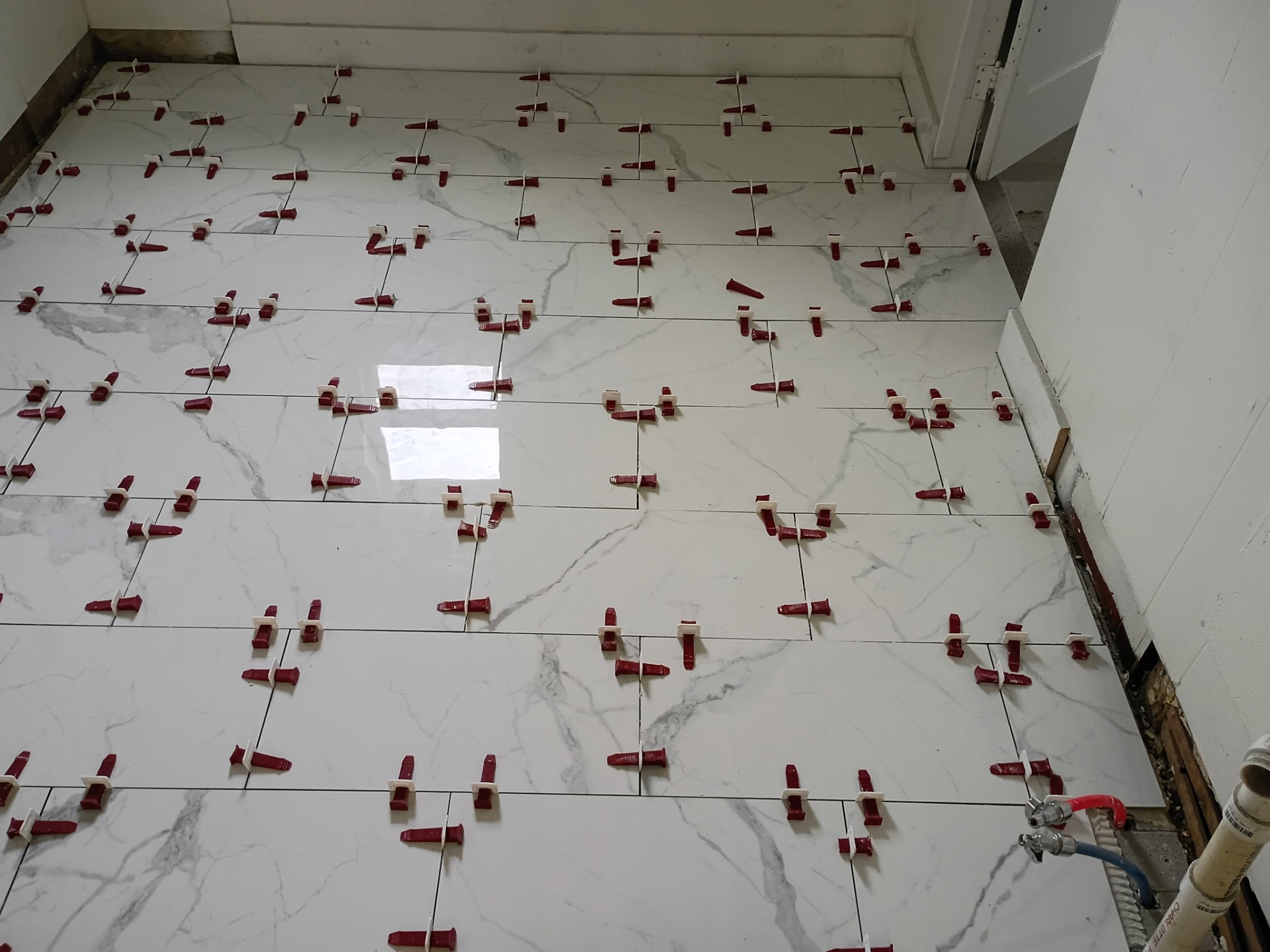 Marble-look porcelain tile floor mid-install with leveling clips and wedges in place